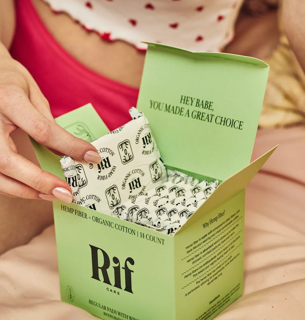 Person holding organic cotton hemp fiber period pad from open green box on bed
