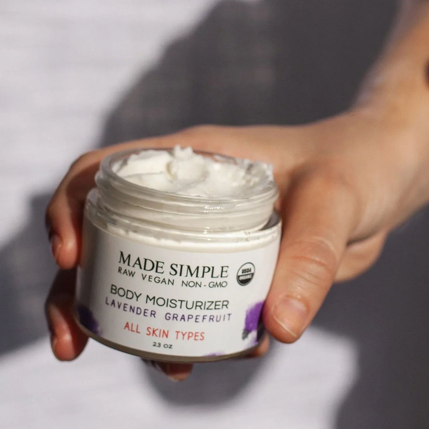 Hand holding a jar of Made Simple lavender grapefruit vegan body moisturizer