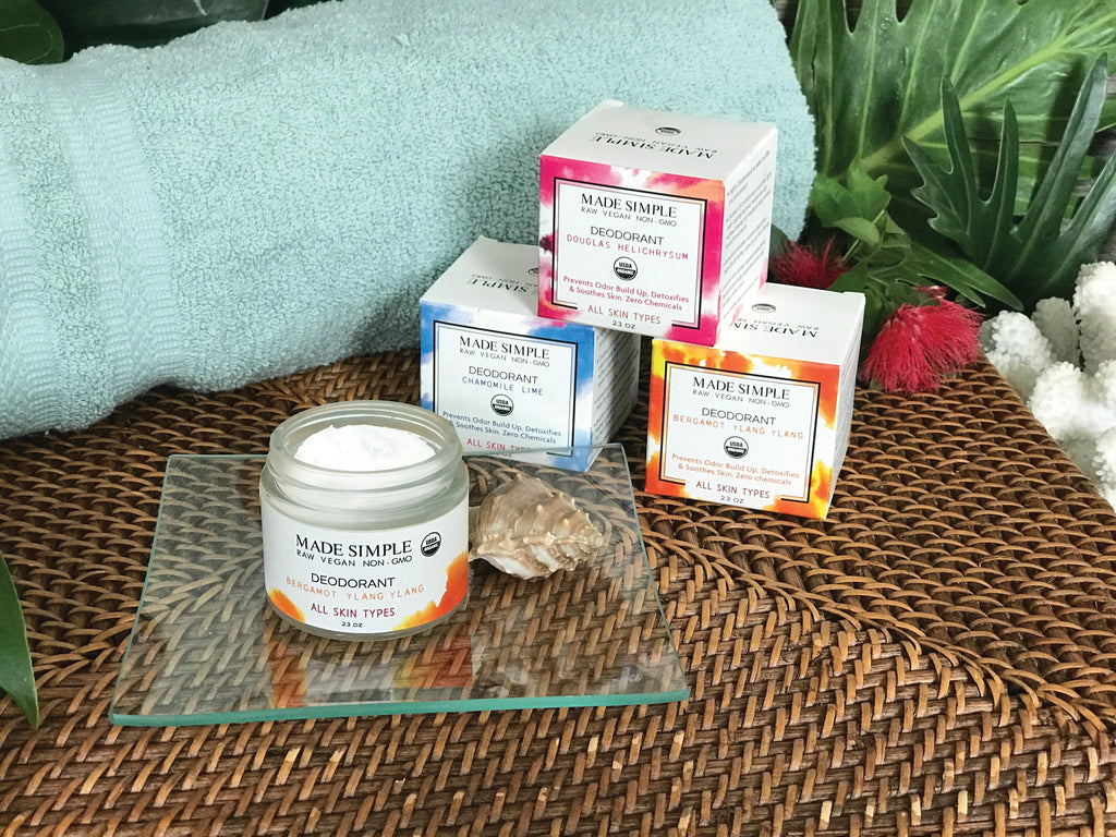 Vegan non-GMO deodorant jars in various scents on a spa-style woven mat with greenery.