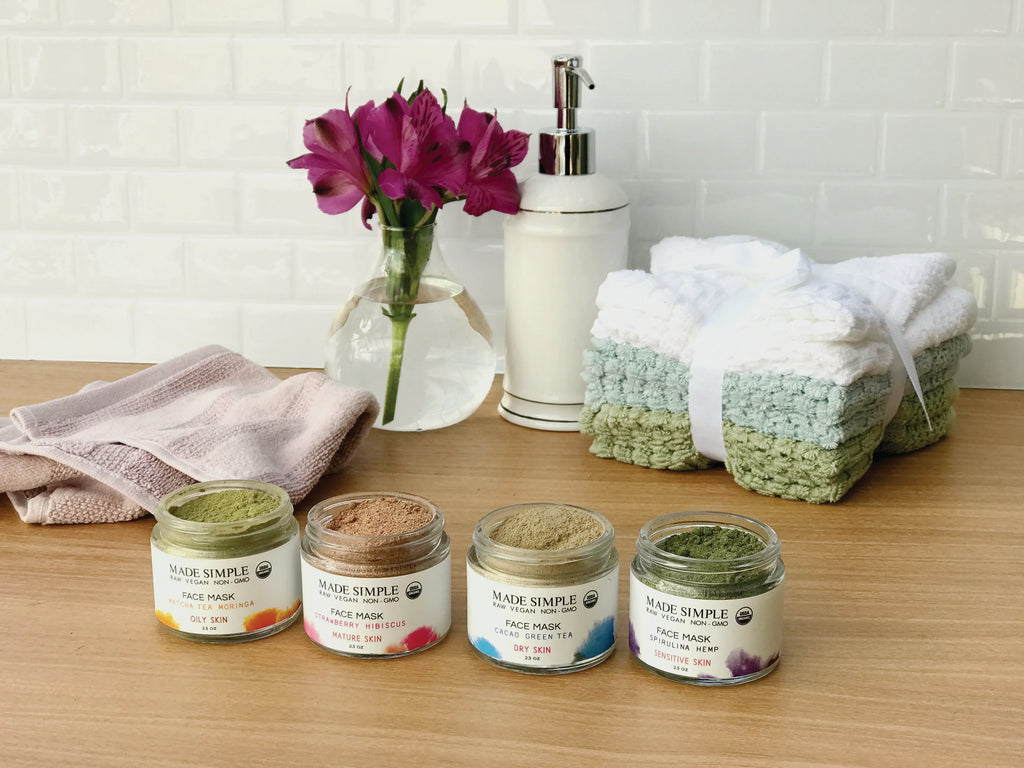 Organic face masks in glass jars with towels, flowers, and soap dispenser on wooden counter