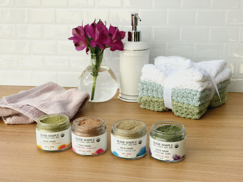 Organic face masks in glass jars with towels, flowers, and soap dispenser on wooden counter