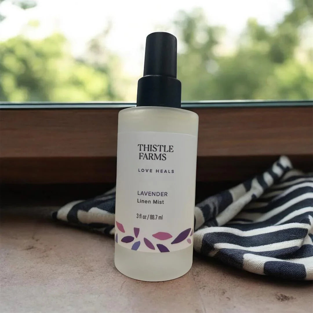 Lavender linen mist spray bottle on windowsill with striped fabric and greenery outside