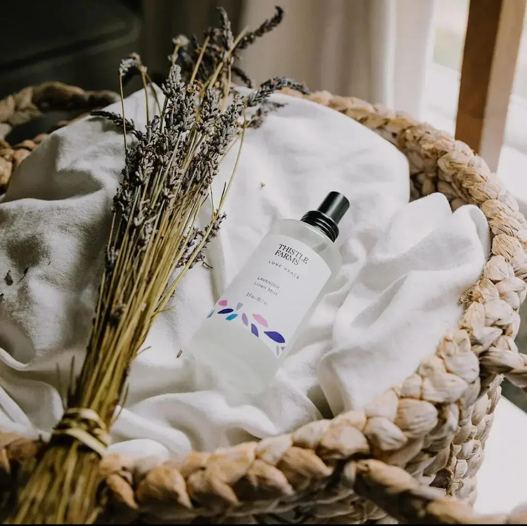 Lavender linen mist spray bottle with dried lavender in a woven basket on white fabric